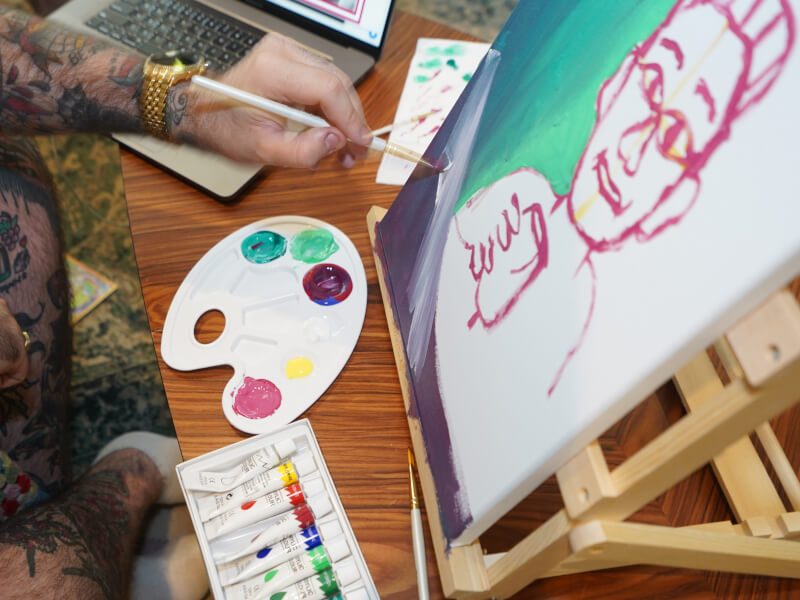 Hands painting a portrait on a canvas with a paint palette